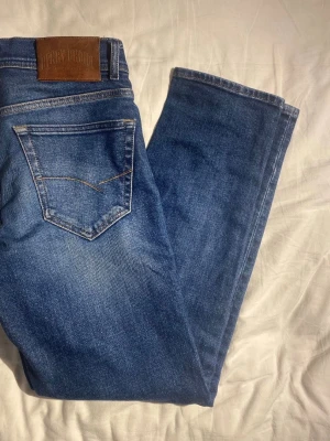 Blå raka jeans från Henry Choice - Säljer ett par klassiska blå jeans från Henry Choice med raka ben och snygga kontrastsömmar. Jeansen har två bakfickor och en läderpatch med logga i midjan. Perfekta till en avslappnad stil och tillverkade i slitstark denim. W27 L30