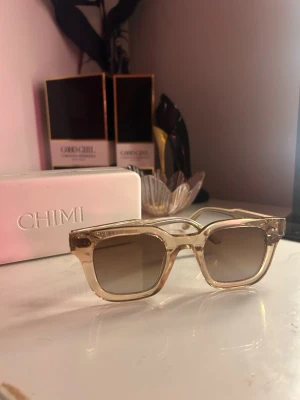Beiga solglasögon från CHIMI  - Säljer ett par trendiga solglasögon från CHIMI med transparent beige båge och fyrkantig form. Glasen är lätt tonade och ger en cool vibe till din look. Perfekta för soliga dagar och kommer med originaletui.