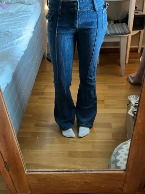 Blå utsvängda jeans med hög midja - Säljer ett par blå jeans med låg midja och utsvängda ben. En knapp på fram fickan har låsnat men annars väldigt bra skick.