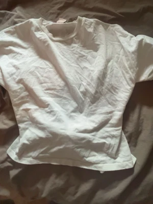 Vit topp med knytband i ryggen - Snygg vit topp med rund halsringning och korta ärmar. Baksidan har ett coolt knytband som ger en unik touch. Perfekt att styla med jeans eller kjol för en fräsch look. Tillverkad i mjuk bomull som känns skön mot huden.