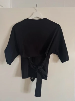 Svart topp med knytband bak - Trendig svart topp från Nelly! Har använt några gånger men den ser helt ny ut!