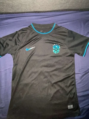 Svart Brasilien Nike fotbollströja - Säljer en svart Brasilien fotbollströja från Nike med blå detaljer och klubbmärke på bröstet. Tröjan har korta ärmar, rund hals och är tillverkad i ett lätt och ventilerande material som passar perfekt till träning eller match.