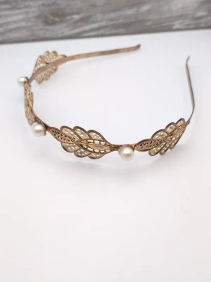 Guldfärgat diadem med pärlor - Snyggt diadem i guldfärgad metall med detaljerade bladformade utskärningar och vita pärlor. Diademet har en elegant och vintageinspirerad design som ger en lyxig känsla. Perfekt accessoar för att lyfta din look.