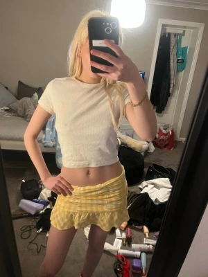 Gul rutig minikjol med volang - Superfin gul och vit rutig minikjol med volangkant. Kjolen har en figurnära passform och är perfekt för dig som vill ha en söt och trendig look. Materialet känns lätt och passar bra till varmare dagar.