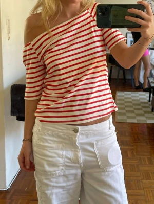 Randig offshoulder topp röd/vit - Trendig offshoulder topp med röda och vita ränder. Kortärmad och croppad modell med avslappnad passform. Perfekt för dig som gillar en avslappnad men snygg stil.