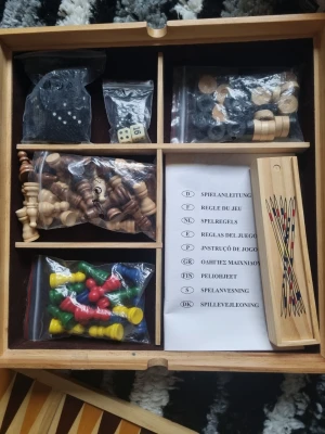 Träspel samling med brädspel - Säljer en träspel samling med flera klassiska brädspel. Setet innehåller spelpjäser i trä och plast, tärningar, schackpjäser, dominobrickor och spelplaner för bland annat backgammon och nio brickor. Allt är organiserat i en trälåda med fack och instruktioner på flera språk.