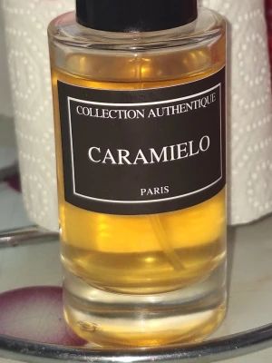 Caramielo Collection Authentique parfym - Caramielo från Collection Authentique Paris är en parfym i en rund, transparent glasflaska med svart etikett och svart lock. Vätskan har en gyllene, karamellfärgad ton som ger ett lyxigt intryck. Perfekt för dig som gillar söta och eleganta dofter.