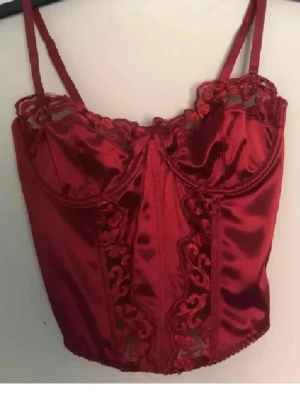 Röd satin korsett med spetsdetaljer - röd korsettopp i glansig satin med vackra spetsdetaljer längs byst och framtill. Aldrig använd endast testad. stretch i den och går att justera banden oxå💕 