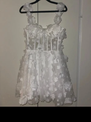 Sommar/studentklänning - Underbar vit klänning med 3D-blommor och korsettliknande överdel. Perfekt till sommarens festligheter eller studentfirandet! Använd endast en gång till studentmottagning och i nyskick. 