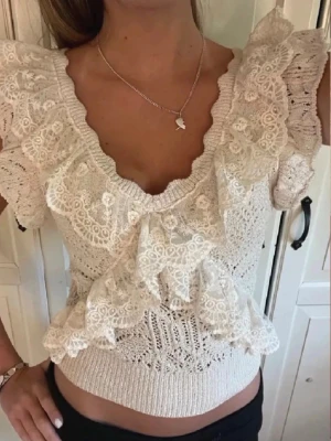 Zara topp  - Supersöt vit blus med v-ringning och stora volanger i spets. Blusen är stickad med detaljer i spets och har korta ärmar. Perfekt för dig som gillar romantisk och feminin stil.