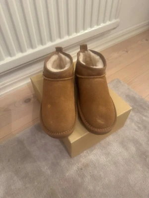 Rugged gear uggs - Mysiga bruna tofflor från rugged gear i mocka med mjukt vitt fårskinnsfoder. Super sköna skor i en fin mellanbrun färg. Skorna är aldrig använda och är i storlek 37, just pågrund av att de aldrig kommit till användning så säljs de för ett rimligt pris!💕