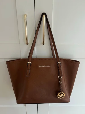 Brun toteväska från Michael Kors - Snygg brun toteväska från Michael Kors i brunt läder. Jag tyvärr inte kvar kvittot! Det är en rymlig väska och en dator får lätt plats samt väldigt mycket mer! Skriv vid minsta fundering! 💕 