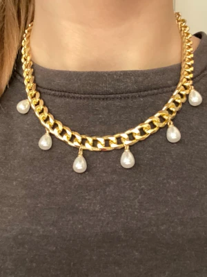 Guldhalsband med droppformade pärlor - Snyggt halsband i guldtonad metall med breda länkar och hängande droppformade pärlor. Perfekt statement piece för att lyfta vilken outfit som helst. Halsbandet har en modern och trendig design som verkligen sticker ut. Jag har gjort det själv!