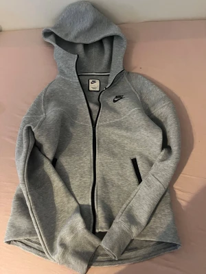 Grå zip-hoodie från Nike - Snygg grå zip-hoodie från Nike med svart dragkedja och svarta detaljer vid fickorna. I storlek S och orginalt köpt för 1000kr pris kan diskuteras. Köpt från dam.