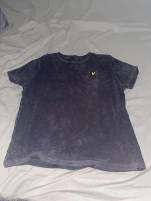 Mörkblå frotté t-shirt från Lyle & Scott - Mjuk och skön mörkblå t-shirt från Lyle & Scott i frotté. Klassisk passform med korta ärmar och rund hals. Bröstet pryds av den ikoniska gula örnloggan som ger en clean och sportig vibe.