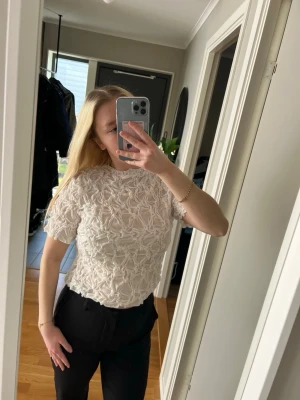 Vit blus med blommönster - Säljer en vit blus med korta ärmar och ett unikt 3D-blommönster över hela tyget. Blusen har en något croppad passform. Är oanvänd endast provad