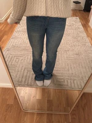 Blå bootcut jeans med brodyr - Snygga blå bootcut jeans med broderad detalj vid fickan och klassisk femficksdesign. Jeansen har en något utsvängd passform nertill och är tillverkade i stretchigt denimtyg för extra komfort.