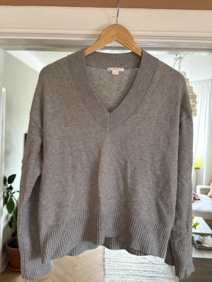 Grå stickad tröja från Gina Tricot - Mysig grå stickad tröja från Gina Tricot med bred ribbad v-ringning, ribbade muddar och nederkant. Perfekt oversized passform för en avslappnad look. Enkel att matcha med jeans eller kjol.