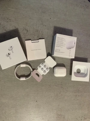 Apple  - Säljer ett par vita Apple AirPods Pro med trådlöst laddningsetui. Hörlurarna har silikonproppar för bättre passform och brusreducering. Medföljer originalförpackning, laddningskabel och extra öronproppar. Snygg och stilren design i blankt plastmaterial.