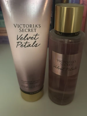 Victoria's Secret Velvet Petals parfymset - Victoria's Secret Velvet Petals parfymset med en rosa body mist och matchande lotion. Flaskan har guldfärgat lock och lotionen kommer i en skimrande rosa tub. Doften är blommig och feminin, perfekt för dig som gillar söta och fräscha toner. Den är Andvänd och inte ny, lite mer än halva parfymen kvar