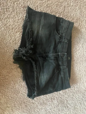 Svarta lågmidjade  jeansshorts - Snygga svarta jeansshorts med fransade kanter och klassisk femficksdesign. Shortsen har låg midja. Rätt stretchigt tyg så passar förmodligen flera storlekar skulle säga ca S-M