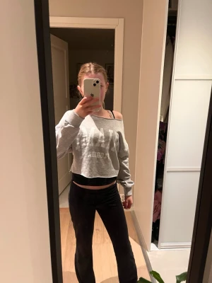 Grå croppad hoodie med tryck - Säljer en grå croppad hoodie med vitt tryck på framsidan. Tröjan har en bred, off-shoulder halsringning och långa ärmar med ribbade muddar. Perfekt för en avslappnad och trendig look.