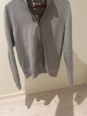 Bläck helzip - En stilren grå ziptröja med hög krage och långa ärmar. Tröjan har dragkedja framtill och ribbade muddar vid ärmslut och nederkant. Perfekt för lager-på-lager och enkel att matcha med olika outfits.