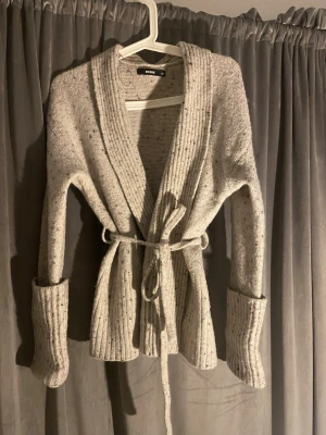 Ljusgrå stickad kofta med bälte BikBok - Stickad Kofta från BikBok, köpt för 600 kr, använd exat 8 gånger, är i fint skick, beige blandad färg. Storlek XS 