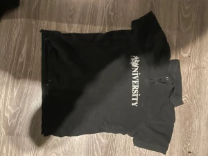 Abn University poli - FIRST ABN DROP Cool svart polotopp med vit text 'UNIVERSITY' på bröstet. Klassisk krage och knappar framtill. Perfekt för dig som gillar en enkel men edgy stil. Materialet känns som bomull och toppen har en normal passning.