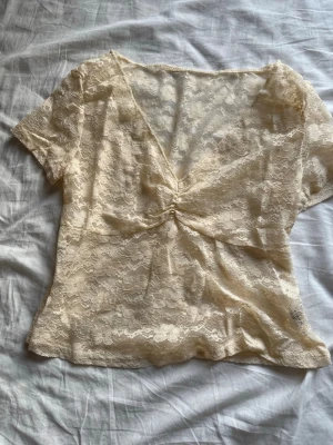 Beige spetsblus med v-ringning - Säljer en superfin beige spetsblus med korta ärmar och v-ringad hals. Perfekt att styla lager på lager eller med ett linne under.