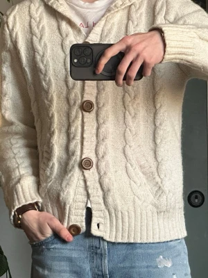 Vit kabelstickad hoodie-kofta - Mysig vit kabelstickad kofta med luva och stora träknappar. Koftan har ribbade muddar och en avslappnad passform, perfekt för lager på lager. Klassisk design med tydliga stickade detaljer och huva för extra komfort. ‼️RACE MARINE INTE RALPH‼️