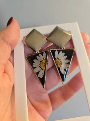 Geometriska örhängen med prästkragar - Unika örhängen i silverfärgad metall med stora geometriska former. Triangelformade hängen med svart botten och inlagda vita prästkragar med gul mitt. Statement-accessoar som verkligen sticker ut och ger en cool retrovibe. Örhängeskrokar rostfritt stål.