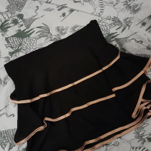 Svart kjol med guldkant - Gammal kjol men aldrig använd. Inga defekter, inte elastisk, har dragkedja. Storlek L