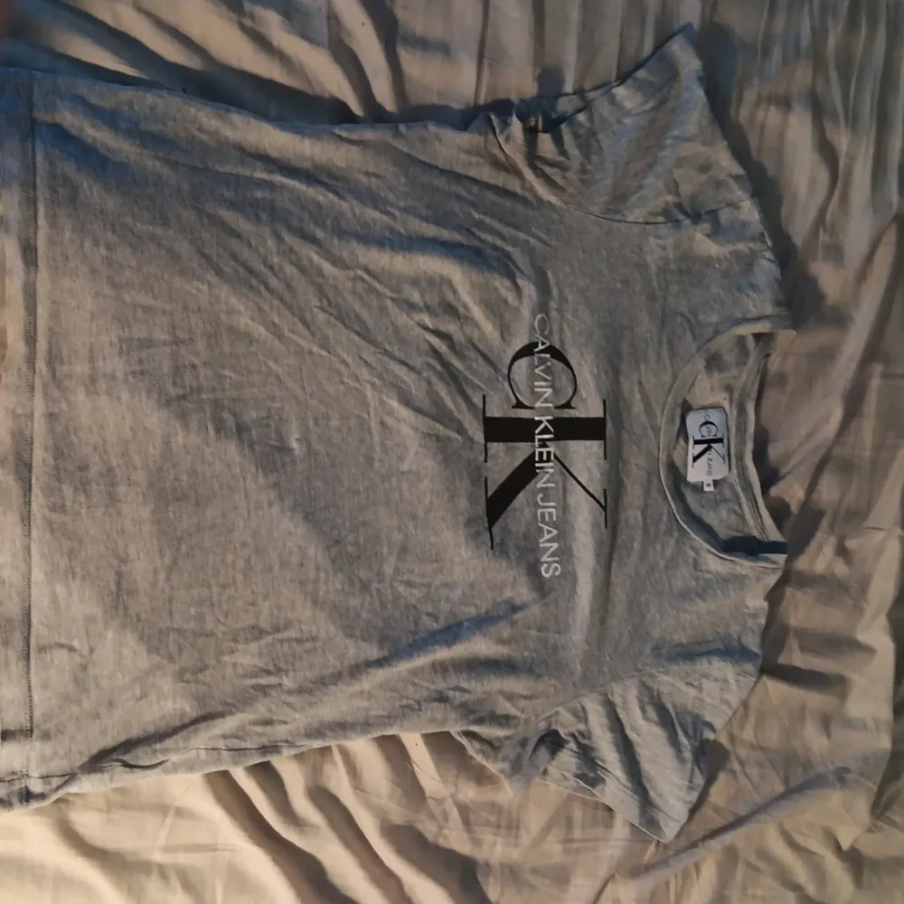 Grå T-shirt från Calvin Klein i storlek S. Väldigt välanvänd, men fortfarande i gått skick. På bild 4-5 ser man en lite fläck vilken drar ner pris och kvalitet.   Material: bomull. T-shirts.