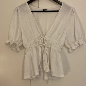 Volangblus från Gina med rosetter  - Supersöt vit volangblus! Materialet har lite egen struktur och knytning i fram som man ser på bilden 