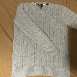 Polo Ralph Lauren tröja - Hej, jag säljer denna baby blå kabelstickade Polo Ralph Lauren tröjan då jag inte använder den längre eftersom att den har blivit för liten. Skicket är 10/10 och den har inga som helst defekter. Storleken är XL i barn men passar som xs och s. 