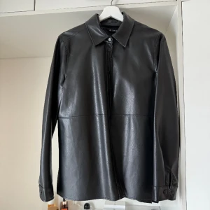 Skinnskjorta från Gina Tricot  - Snygg skjorta i fusk skinn från Gina Tricot. Storlek 36 men funkar som en 38a likaså då jag upplever den stor. Knappt använd! 