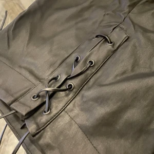 Oanvända nyskick skinnbyxa i svart. Byxa med snörning  - Helt nya ”skinn/läder” byxor me snörning ifram