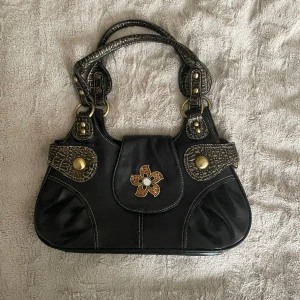 Axelväska  - Väska med mycket detaljer i konstläder.