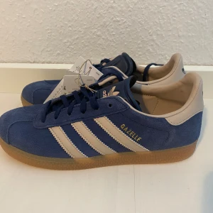 Nya retro Adidas Gazelle - storlek 36 2/3 - Adidas originals gazelle j i storlek 36 2/3 Färgen är marinblå och beige (night indigo/wonder taupe) Nya och oanvända med tags.  Populär färg med vintage inspiration.  Slutsålda.  Handball Spezial Samba