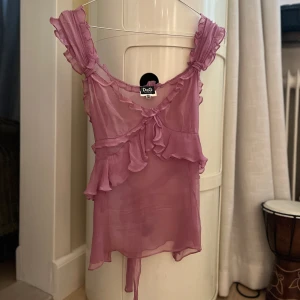 Dolce & Gabbana topp - Lila linne/blus från Dolce & Gabbana. Toppen skick med vackra volanger. Dragkedja i sidan för att enkelt få på och av toppen samt ett knyte i rygg som även går att knytas fram. Storlek är en italiensk 26/40. Runt XS (jag bär S/36kr