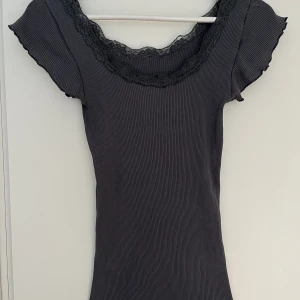Mörkgrå kortärmad topp spelskant S - Supersöt, mörkgrå topp med kort ärm, rund halsringning med spetskant. Ribbstickad i fin ä, skön kvalitet. Bra skick. Material, märke och storlekslapp saknas men känns som silkesmix.