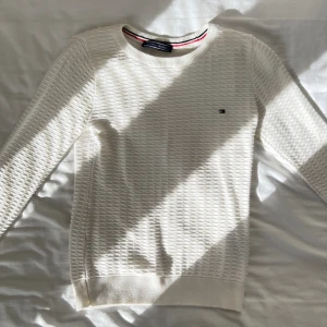 Tommy Hilfiger vit tröja - En vitt Tommy Hilfiger tröja. Medel lång vid höfterna. Ett märkes logo på bröstet. Långärmad. Äkta eller inte? Troligen inte!! Fick den köpt utomlands år tillbaka. Använt den lite & säljer tröjan för det inte riktigt är min still. Den är i bra skick.