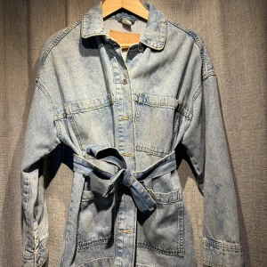 Jeansjacka H&M -  Jeansjacka från H&M med bälte i midjan. Använd men i gott skick! Något stor i storleken. 