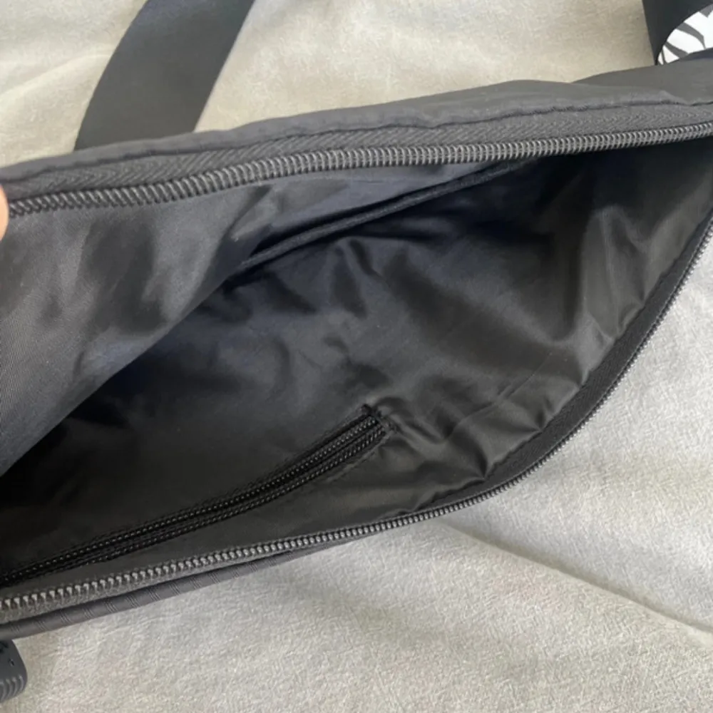 En liten svart magväska med mycket utrymme. Väskor.