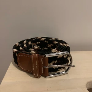 Flätat Grich Bälte - 120cm långt, helt nytt. Bältet är svart, beige och brunt passar bra med jeans.