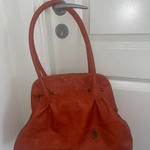 Orange väska  - Höjd: 27 cm Bredd: 38 cm (botten)  Djup: 8 cm (botten) Använd gärna köp nu knappen.