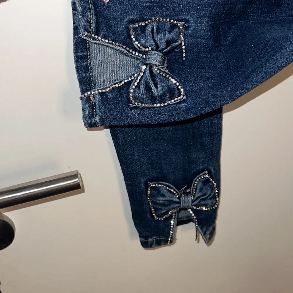 Ett par marinblåa skinni jeans från Redial Paris med rosetter på anklen. Storlek xs/34. (Väl använda). Rosetternas pärlband är lite av samt knappen på framsidan sitter lite löst med den går att laga. . Jeans & Byxor.