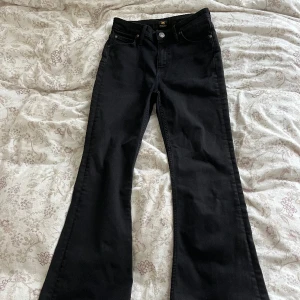 Svarta bootcut jeans från Lee - Svarta jeans från Lee i storlek W28 L31. De är i bra skick förutom att de är lite trasiga där nere (se på bild 3). Innerbenet är 74 cm och midjemåttet rakt över är 32 cm. Tryck gärna på köp nu!❤️