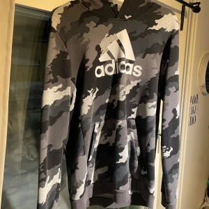  Hoodie med ficka vid magen Adidas  -  Denna Adidas hoodie har en öppen ficka i magen och och är färdig kombinerad med grå ljusgrå svart och små mörkblå detaljer jag kände att den här tröjan inte var något för mig och hoppas kanske kommer någon annan:)